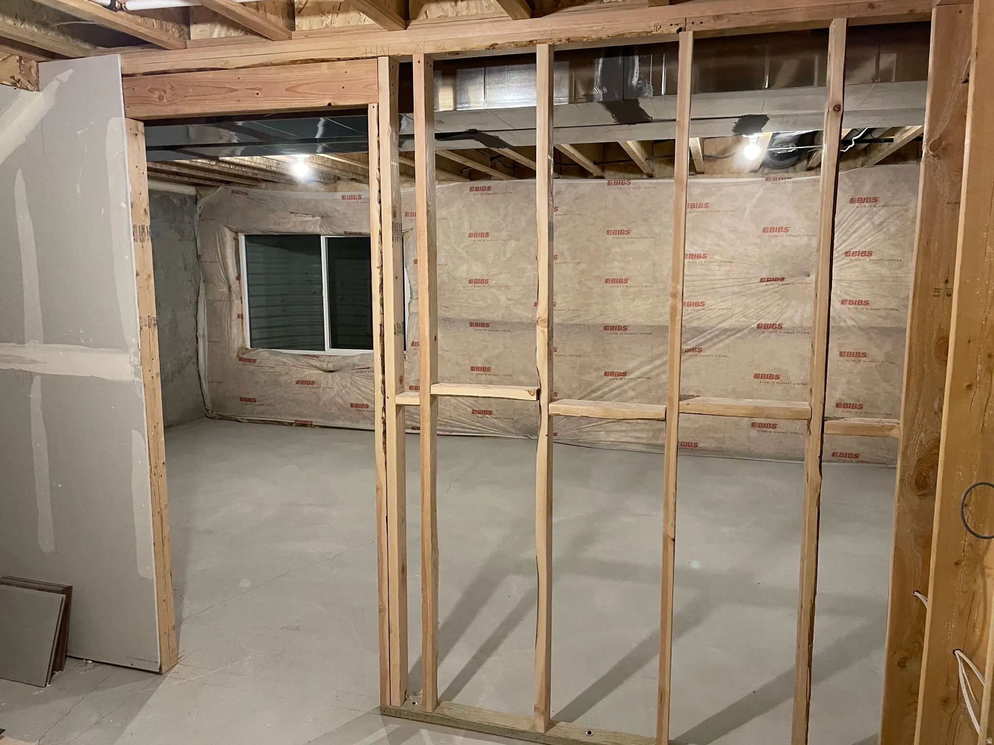 Unfinished interior space with exposed wood framing, concrete flooring, and an egress window