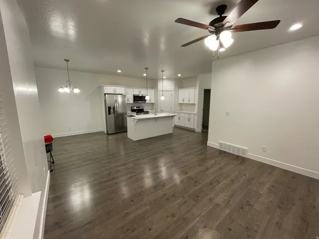 Open-concept living area featuring wood-finish flooring, a contemporary ceiling fan, and a kitchen with white cabinetry, stainless steel appliances, and an island