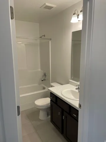 White tile flooring with a dark wood-finish vanity, white countertop, and integrated sink
