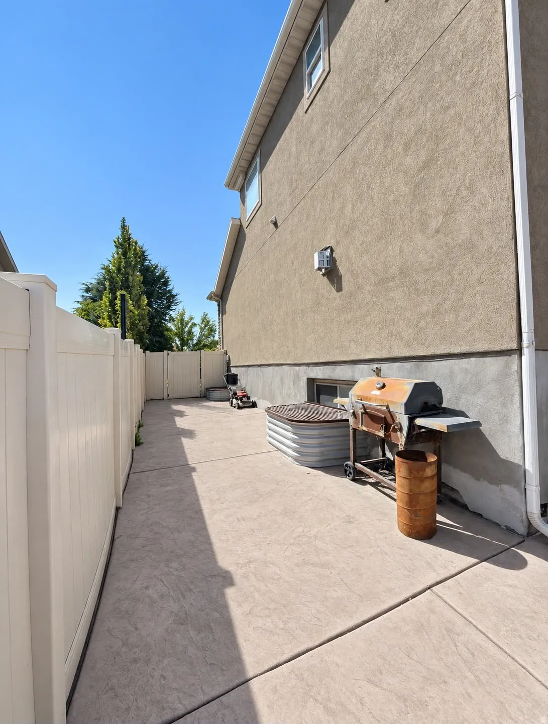 Exterior featuring stucco siding, white vinyl fencing, and concrete hardscaping