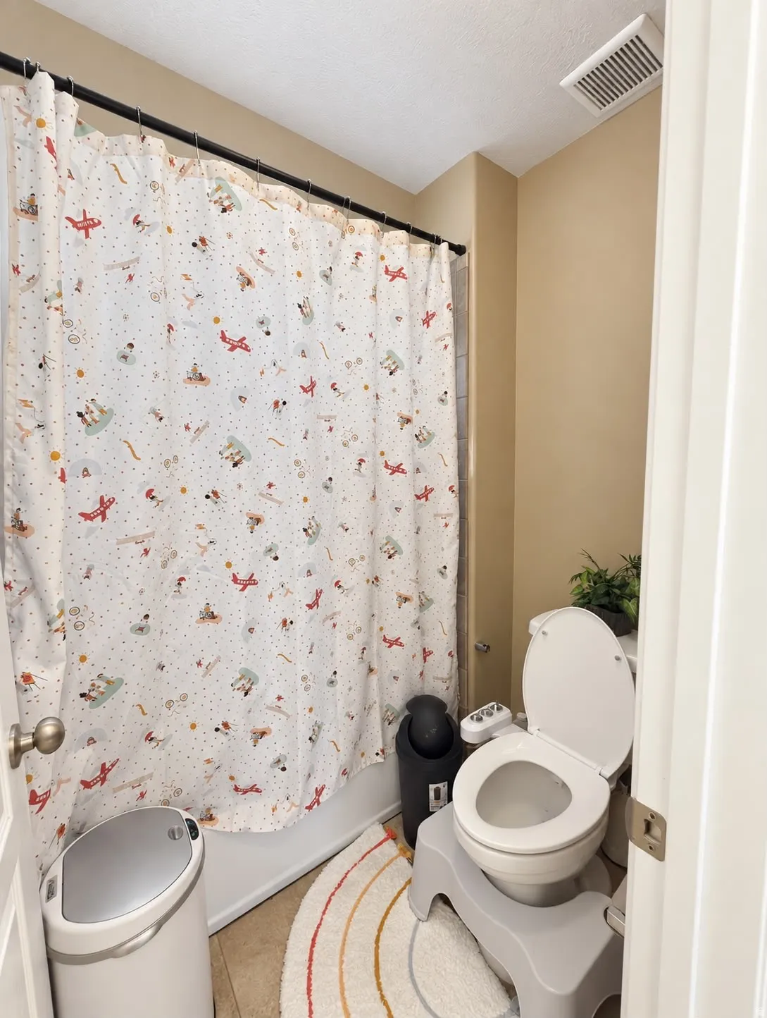 Tub and shower combination with a black shower curtain rod, a white toilet, and tile flooring