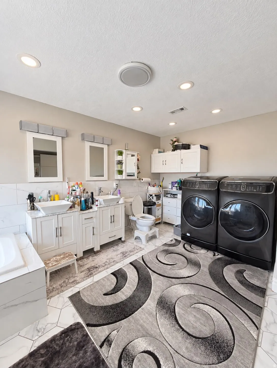 Dual vanity with vessel sinks, white cabinetry, recessed lighting, and a built-in laundry area