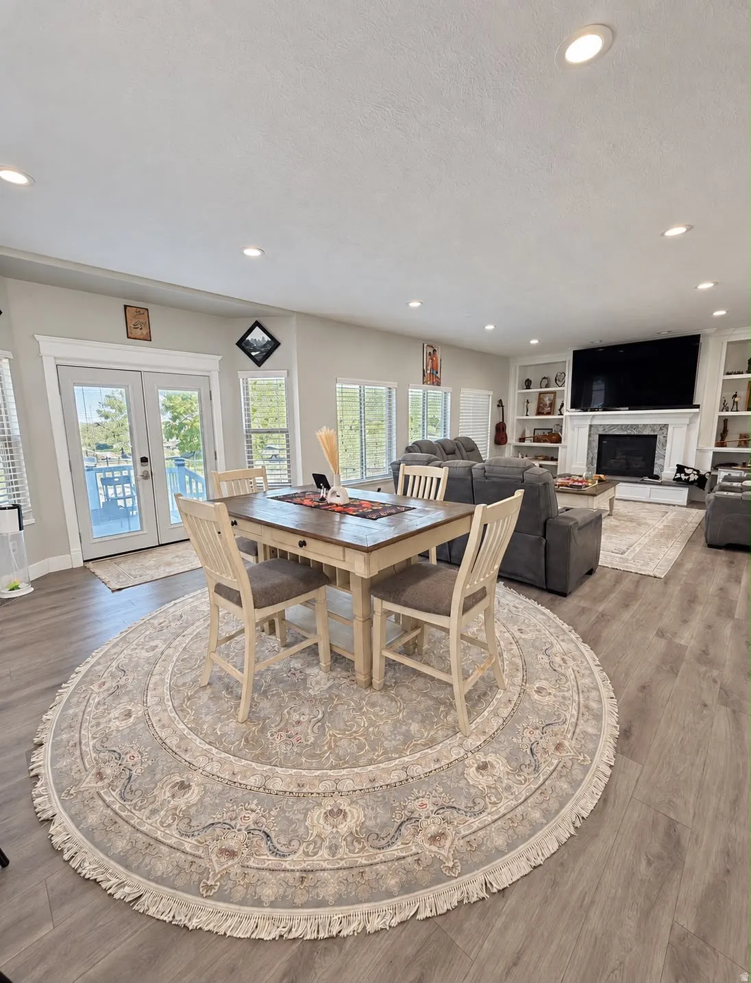 Recessed lighting throughout, wood-finish flooring, built-in shelving, fireplace with stone surround, and French doors
