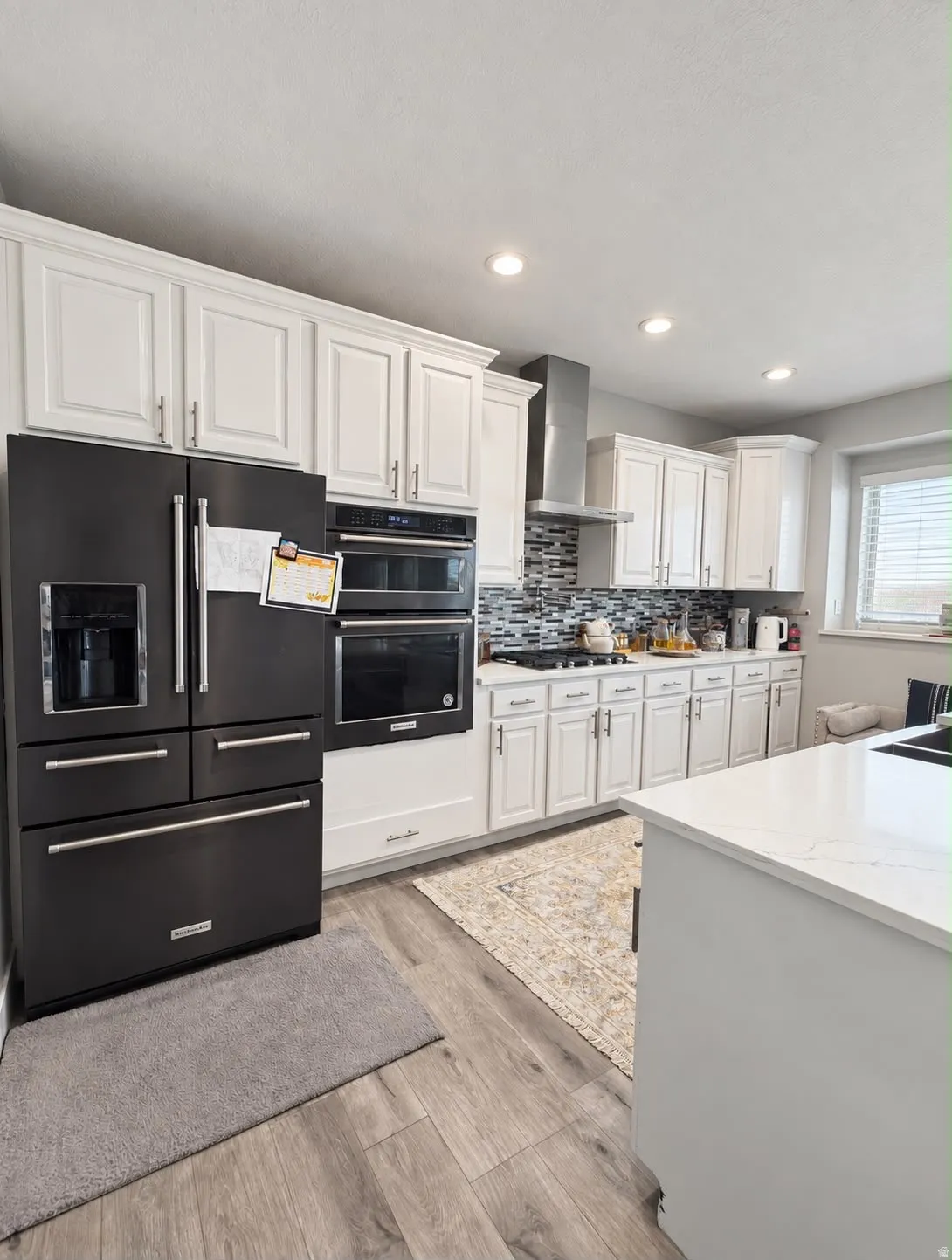 Kitchen featuring white cabinetry, built-in stainless steel appliances, wood-finish flooring, and a stone-finish island countertop