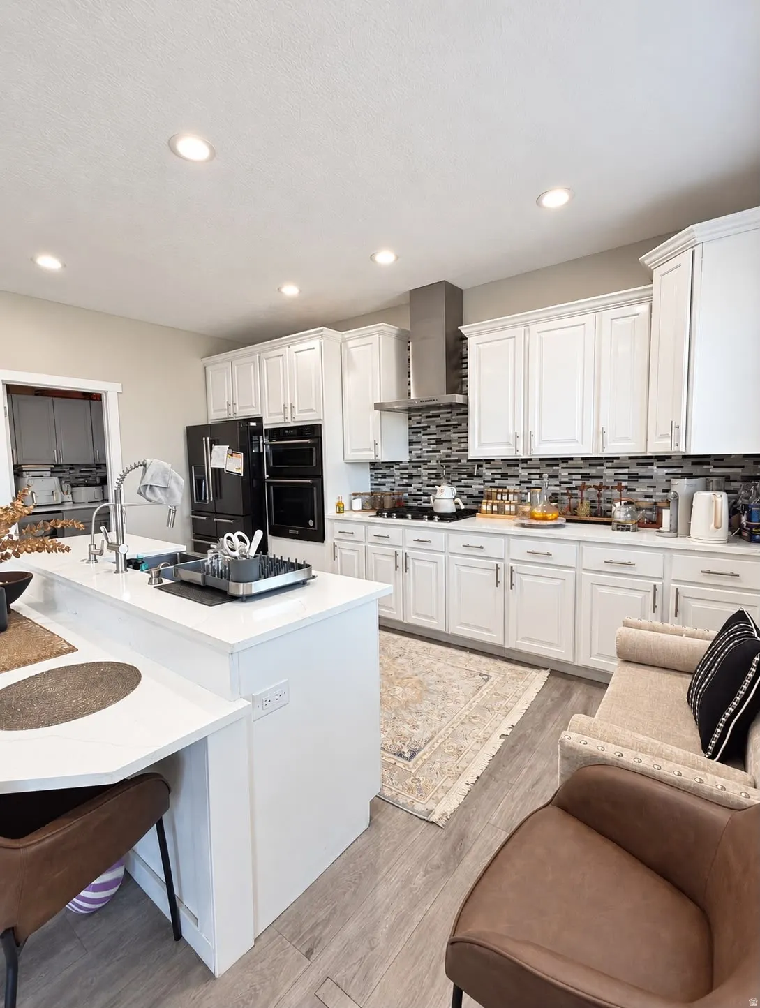 Kitchen with recessed lighting, white cabinetry, a stainless steel range hood, mosaic tile backsplash, and wood-finish flooring