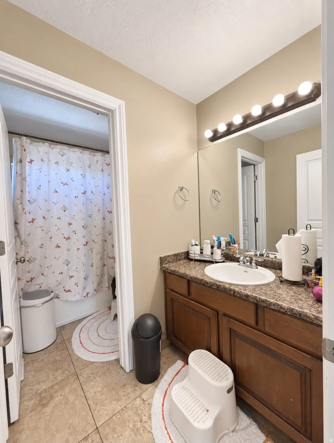 Vanity with integrated sink, wood-finish cabinetry, stone-finish countertop, full-width mirror, and overhead strip lighting
