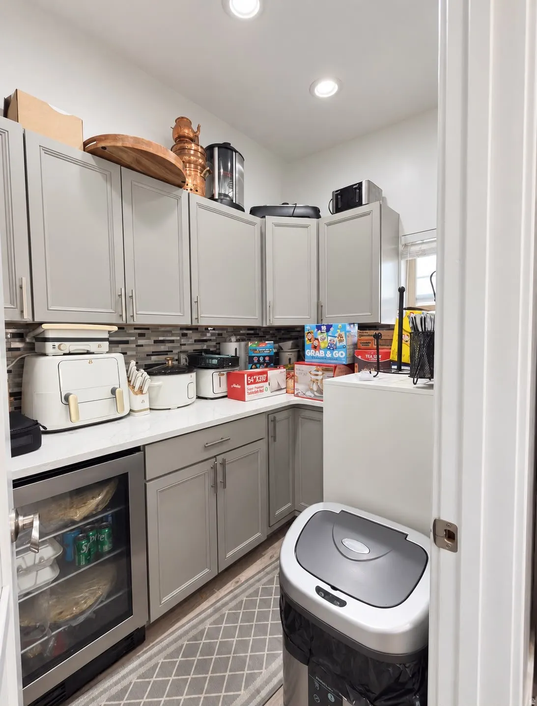 Built-in beverage refrigerator, white countertops, grey shaker-style cabinetry, recessed lighting, and a backsplash with varied tile