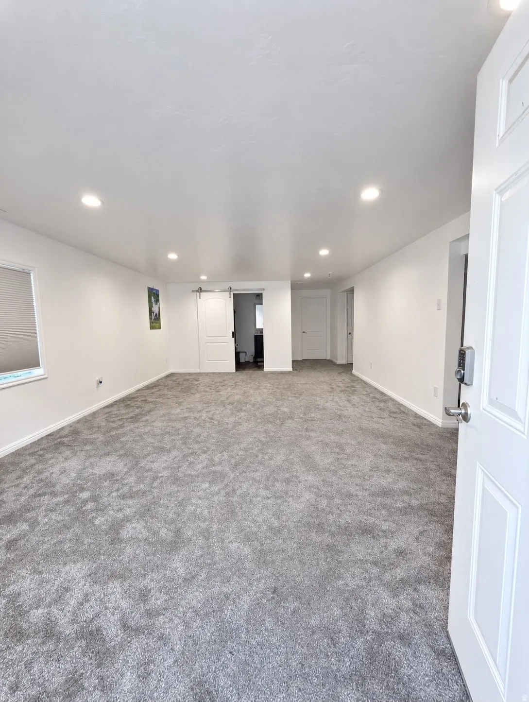 Spacious interior with gray carpeting, recessed lighting, and a white barn door