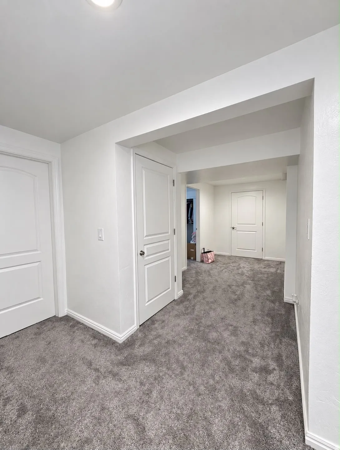 Recessed lighting illuminates fresh white walls and plush gray carpeting, complemented by white paneled doors