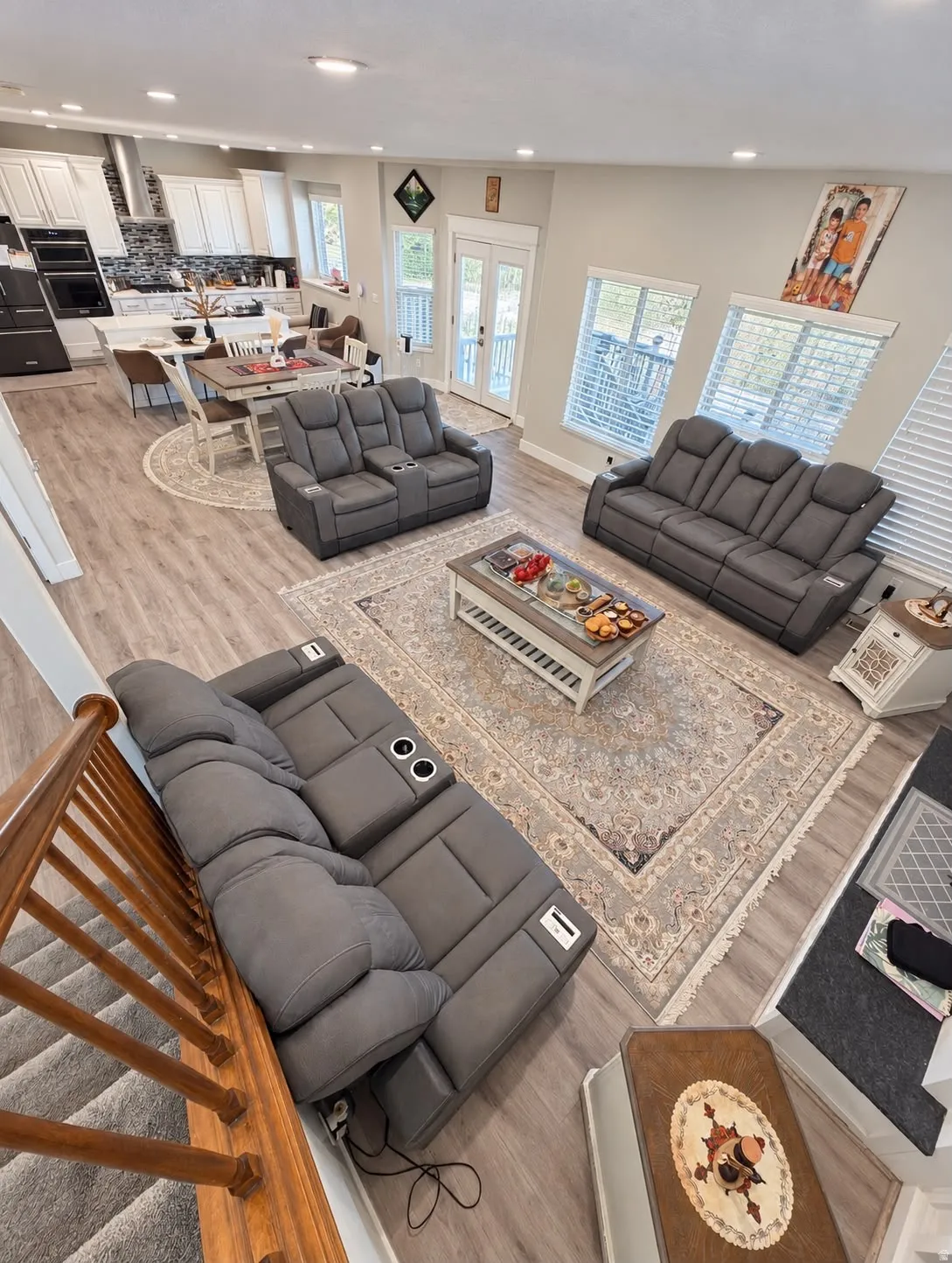 Open-concept living space with wood-finish flooring, recessed lighting, and a modern kitchen featuring white cabinetry, a large island, and stainless steel appliances