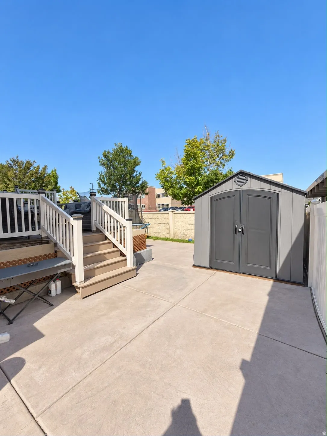Paved patio area, multi-level composite deck with white railings, and a gray storage shed