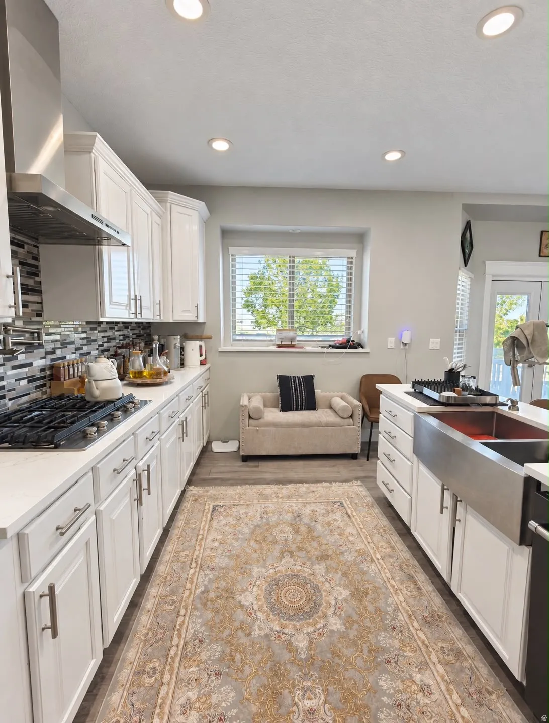 White shaker cabinetry with brushed nickel hardware, stainless steel apron-front sink, gas cooktop with stainless steel range hood, and recessed lighting