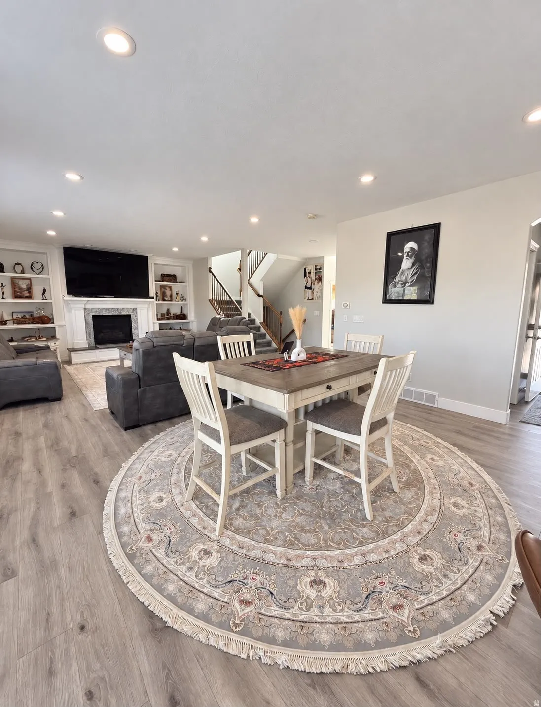 Recessed lighting, wood-finish flooring, staircase with dark wood-finish handrail, white painted built-in shelving, and a fireplace with a white mantel and surround