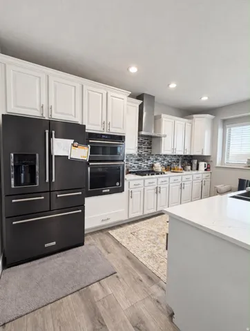 Kitchen featuring white cabinetry, built-in stainless steel appliances, wood-finish flooring, and a stone-finish island countertop