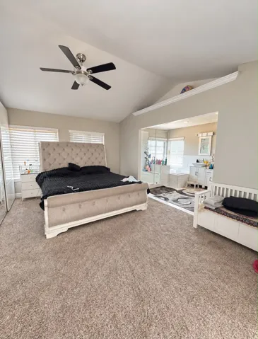Vaulted ceiling with a ceiling fan, carpeted flooring, and an open doorway to an adjoining room