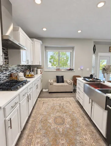 White shaker cabinetry with brushed nickel hardware, stainless steel apron-front sink, gas cooktop with stainless steel range hood, and recessed lighting