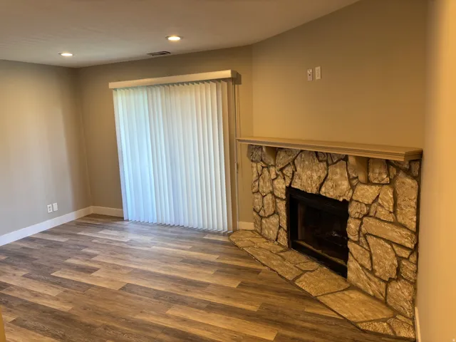 Stone-surround fireplace with a wood mantle, wood-finish flooring, recessed lighting, and vertical blinds