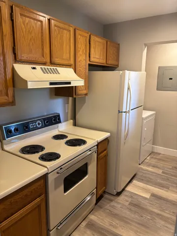 Kitchen featuring wood cabinetry, solid surface countertops, white appliances, and wood-finish flooring