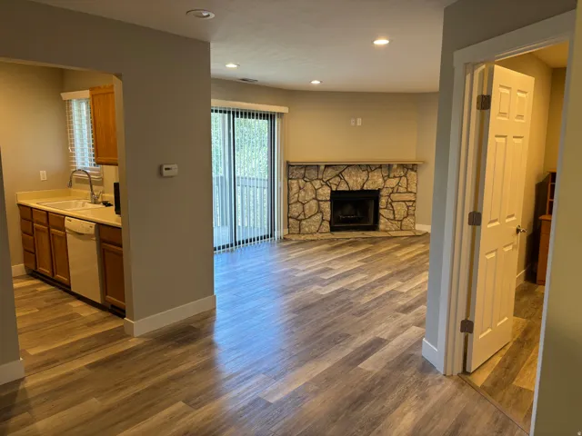 Spacious living area featuring wood-finish flooring, a stone-clad fireplace, recessed lighting, and a sliding glass door to an outdoor area