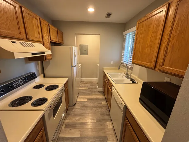 Kitchen featuring wood cabinetry, light-toned countertops, a white electric range, a white refrigerator, and wood-finish flooring