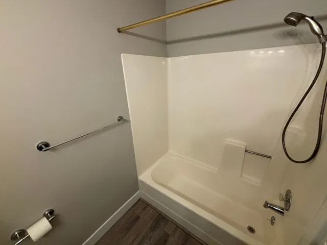 Tub/shower combination with a handheld showerhead, chrome fixtures, and wood-finish flooring
