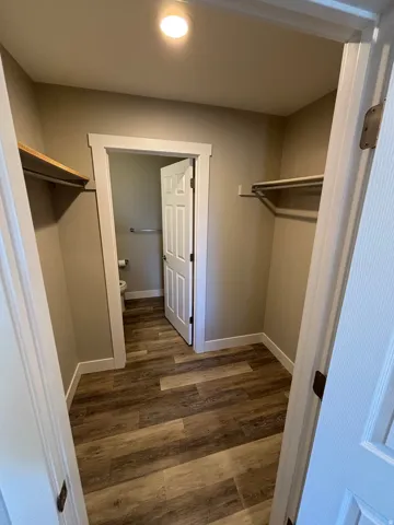 Recessed ceiling light, wood-finish flooring, white trim, and built-in shelving with hanging rods