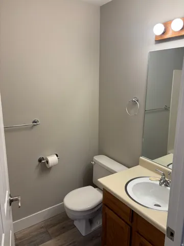 Powder room featuring a wood-finish vanity with an integrated sink, a wall-mounted mirror, and wood-look flooring