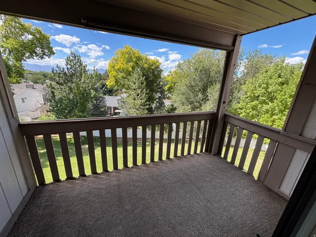 Balcony with textured carpeting, wooden railing, and slatted soffit