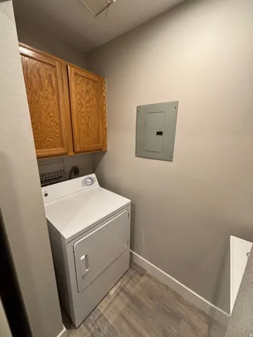Laundry area with overhead wood-finish cabinetry and wood-finish flooring