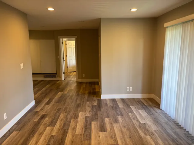 Wood-finish flooring throughout, neutral wall tones, recessed lighting, and white vertical blinds
