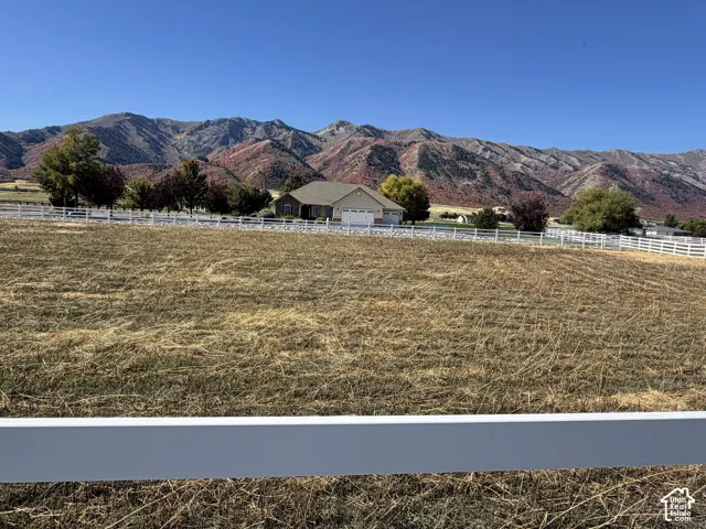 Expansive lot featuring a white fence, scattered trees, and a distant single-story residence with an attached garage