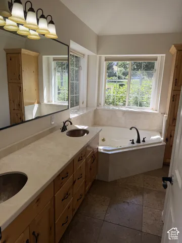 Dual vanity with copper vessel sinks, an integrated jetted tub, tile flooring, and two windows with natural light