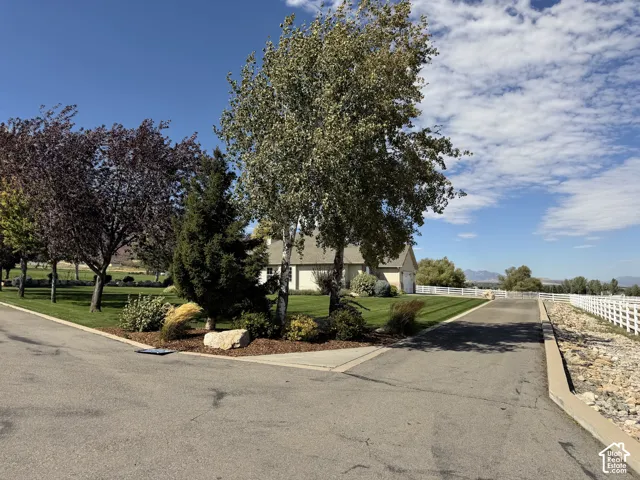 Expansive grounds featuring a manicured lawn, mature trees, white fencing, and a paved driveway
