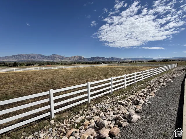 Expansive open field with a white rail fence, a gravel and rock border, and distant mountain range