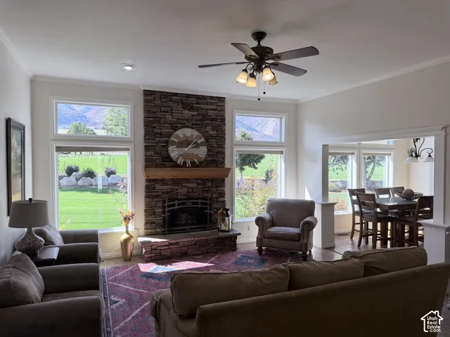 Stone-clad fireplace with a wood mantle, ceiling fan with integrated lighting, recessed lighting, crown molding, and large windows with transom elements and stunning views!