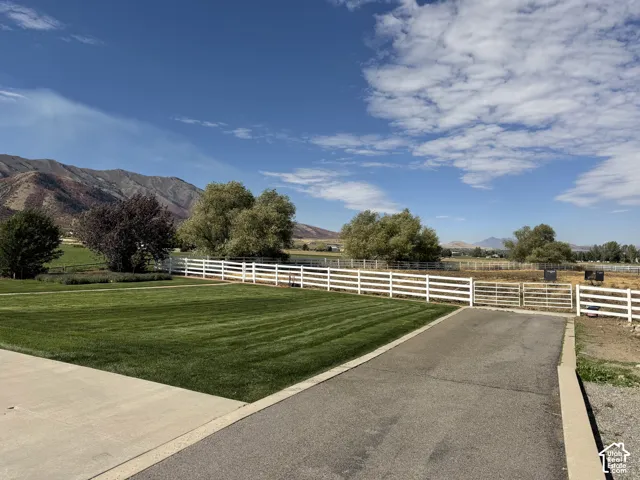 Expansive green lawn with a white fence perimeter, asphalt driveway, and a mountain backdrop