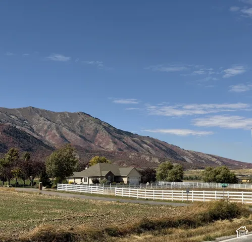 Expansive property featuring a white 3 rail vinyl fence, mature trees, and a mountain backdrop