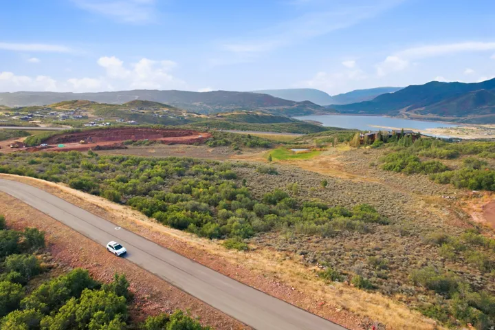 Paved road with surrounding natural vegetation, distant water body, and mountainous terrain