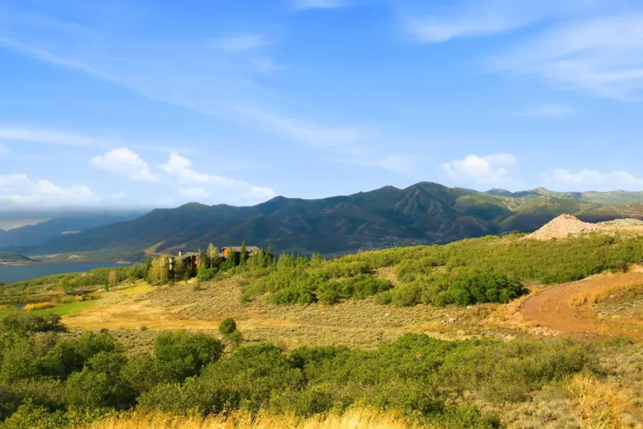 Expansive mountain landscape with a visible body of water, distant mountain range, and varied natural foliage