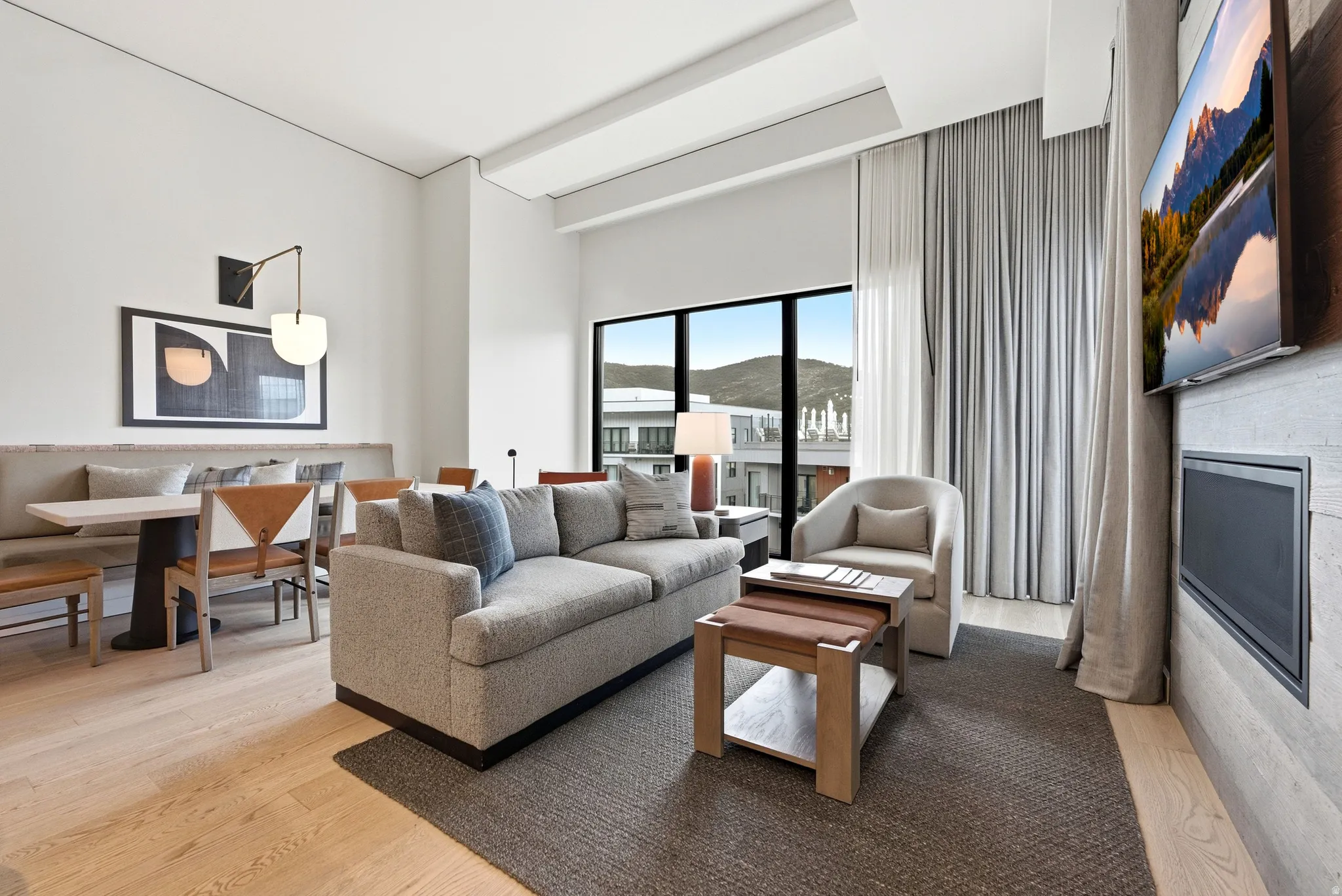 Open-concept living area with light wood-finish flooring, a contemporary fireplace, and a large window