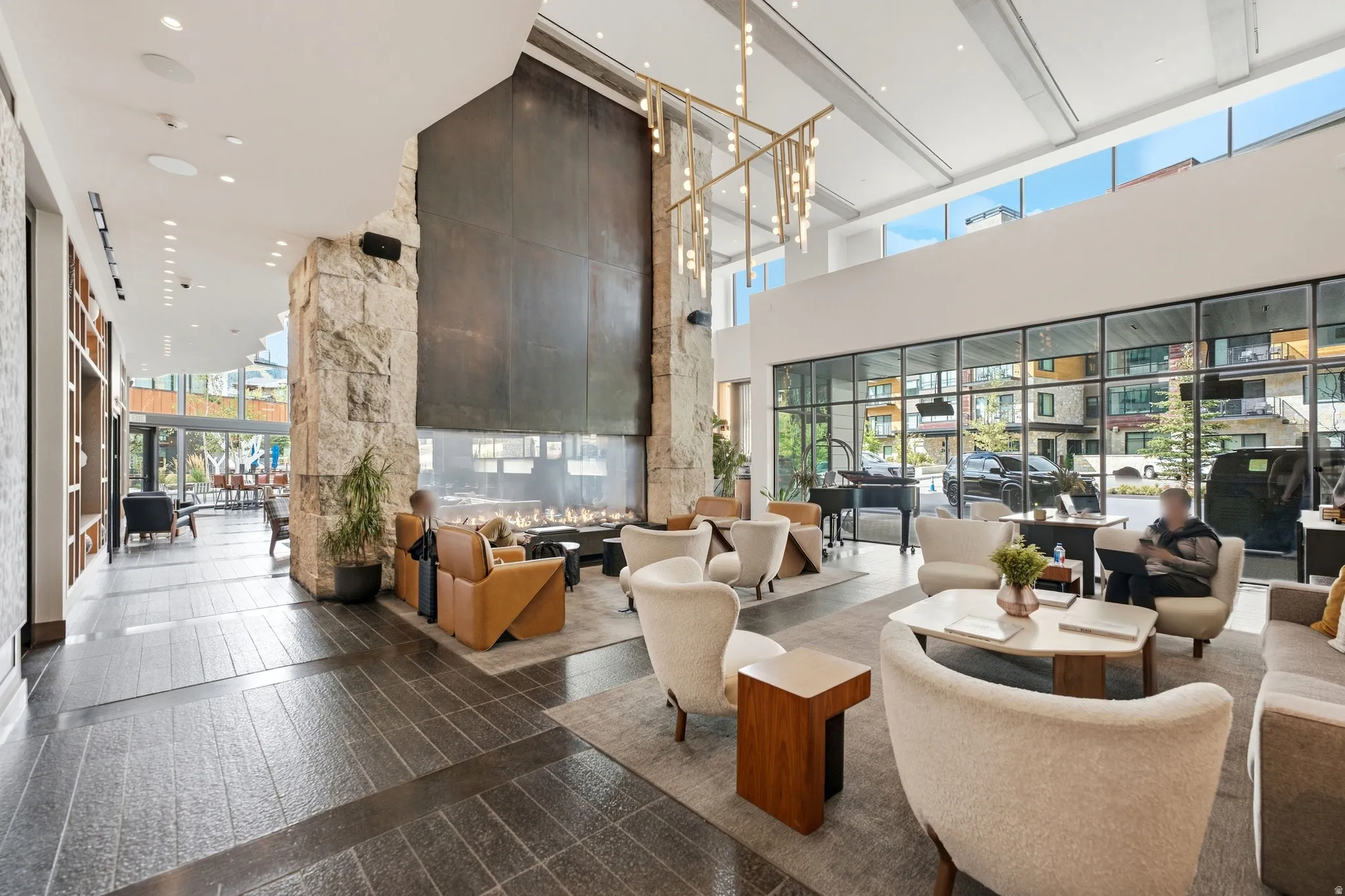 Spacious lounge area featuring a large fireplace, stone accent walls, expansive windows, and sophisticated overhead lighting
