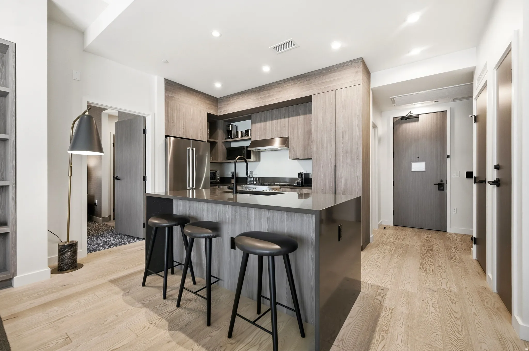 Modern kitchen featuring light wood-finish flooring, an eat-at island with a dark countertop, wood-finish cabinetry, and stainless steel appliances