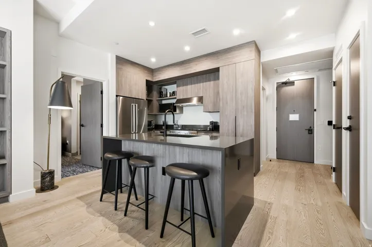 Modern kitchen featuring light wood-finish flooring, an eat-at island with a dark countertop, wood-finish cabinetry, and stainless steel appliances