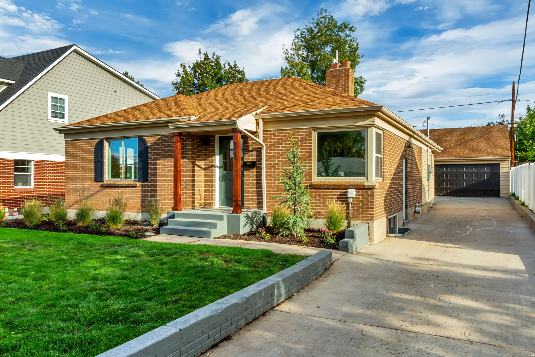 Brick exterior, front porch with wood columns, arched window with shutters, concrete driveway, and detached garage