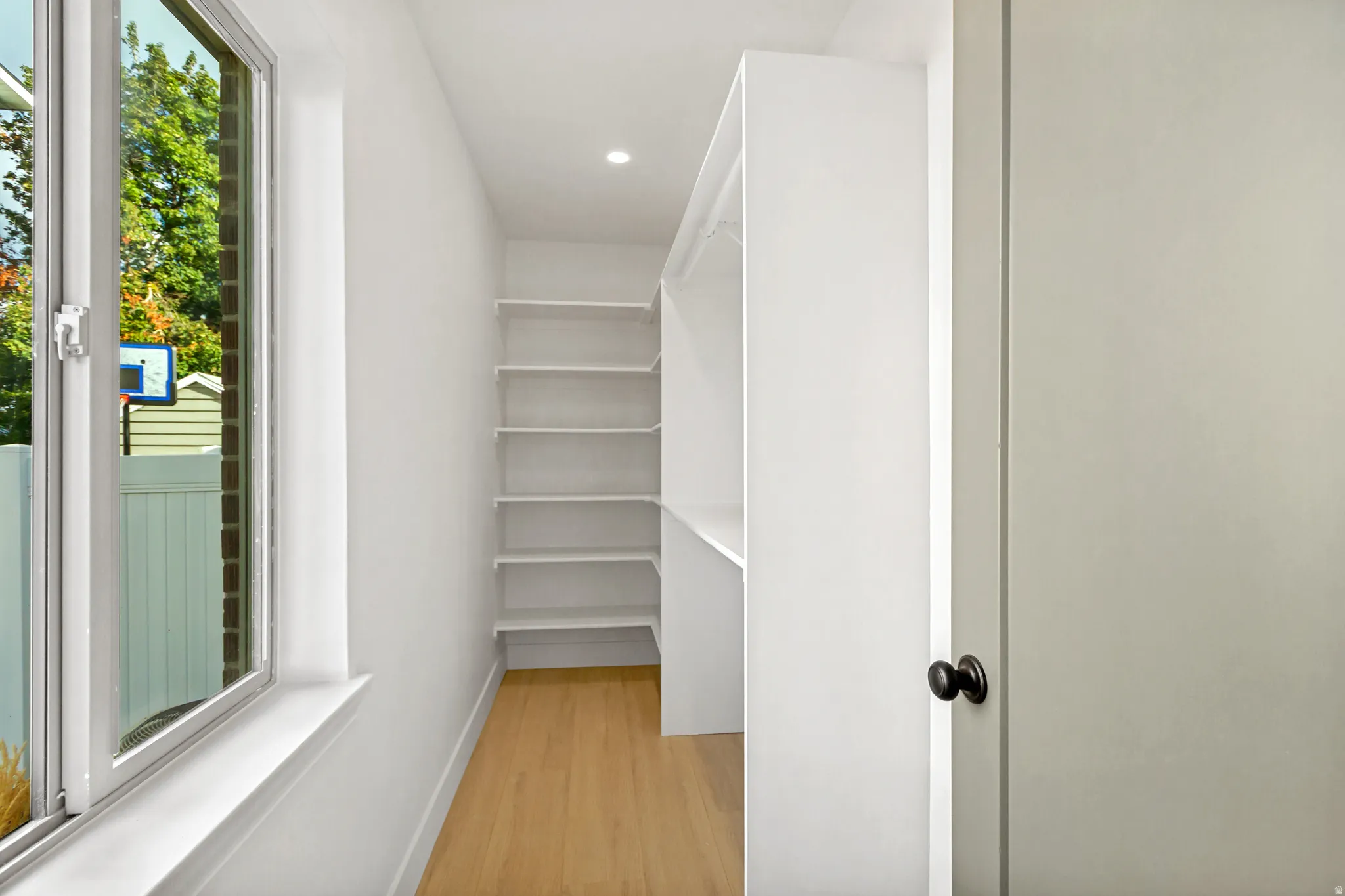 Recessed lighting illuminates wood-finish flooring in this space featuring a large window, built-in shelving, and a built-in hanging rod