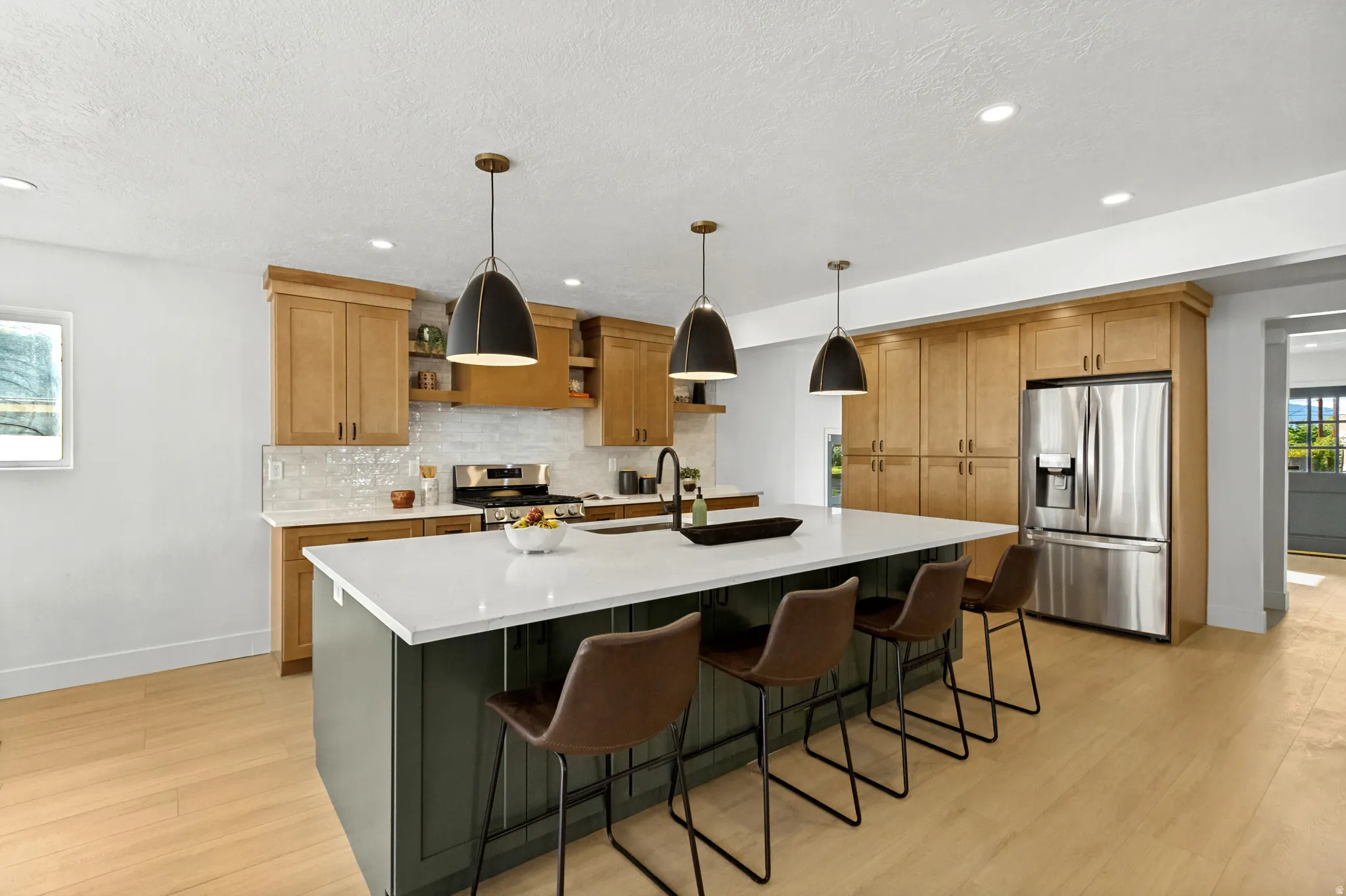 Central kitchen island with white countertop, recessed lighting, wood-finish flooring, stainless steel refrigerator, and pendant lighting fixtures