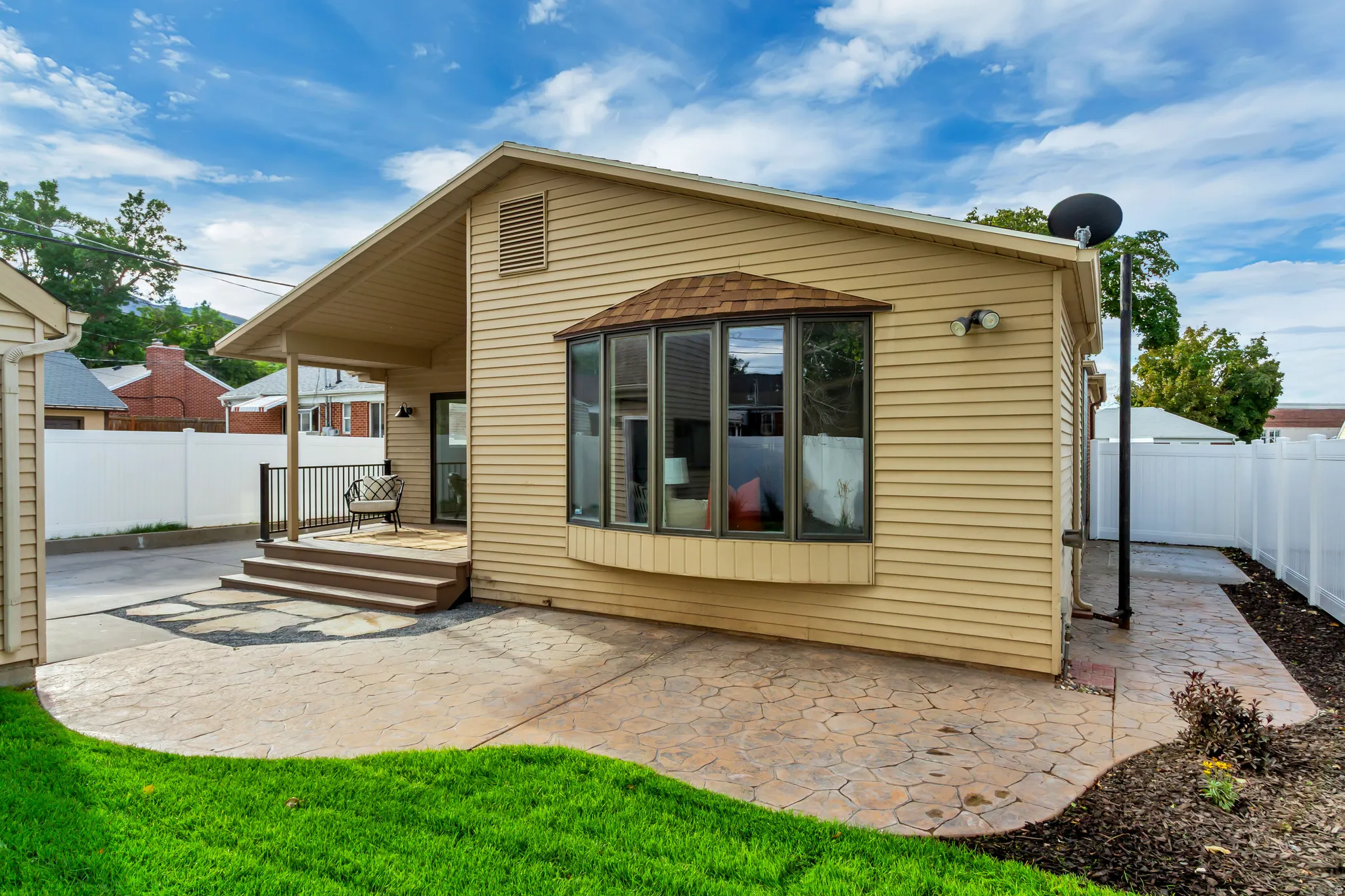 Exterior featuring horizontal siding, a covered deck with railings, a bay window, a patterned concrete patio, and a white vinyl privacy fence