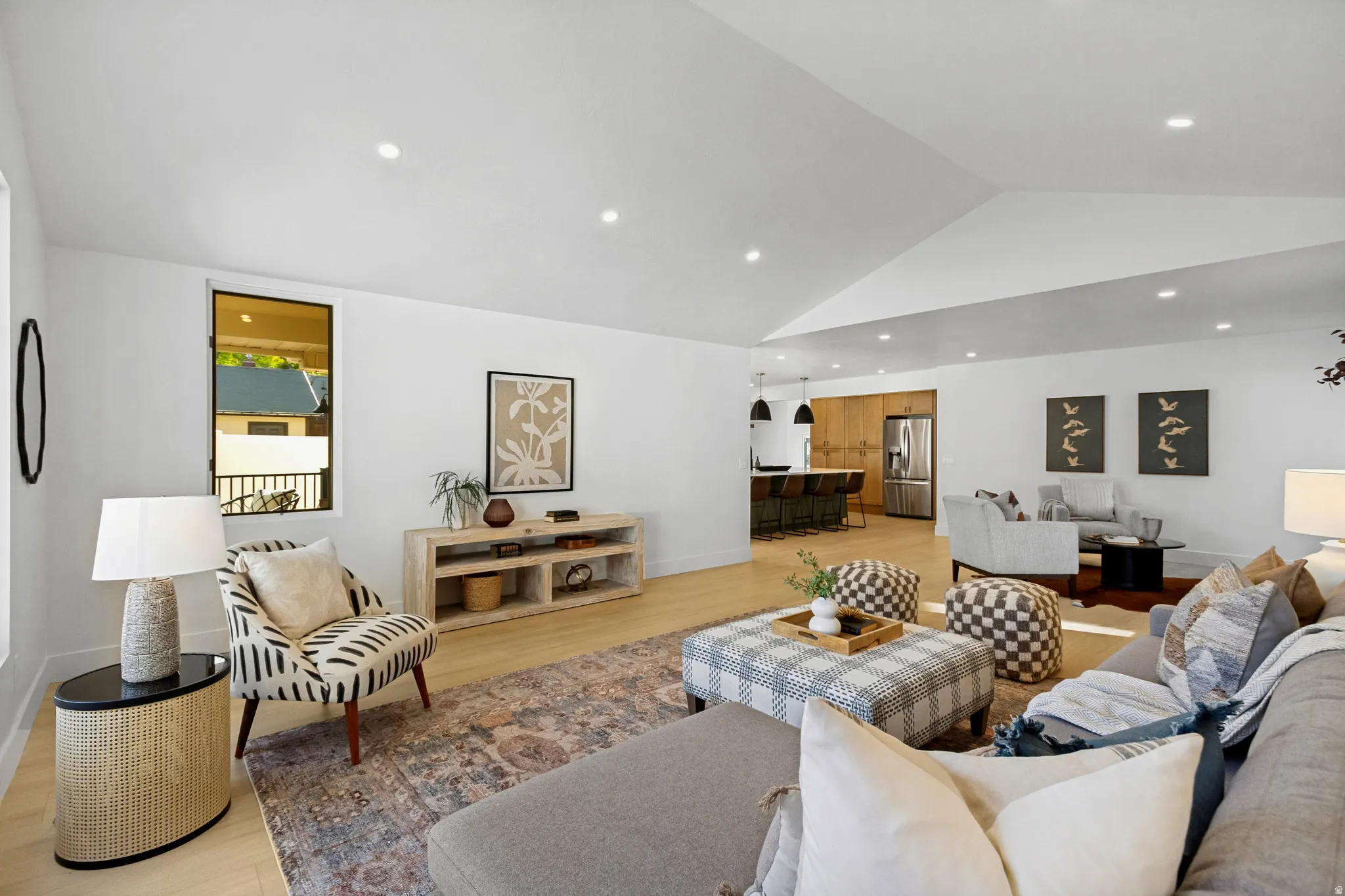 Expansive open-concept living space with vaulted ceilings, recessed lighting, wood-finish flooring, and a kitchen featuring stainless steel appliances