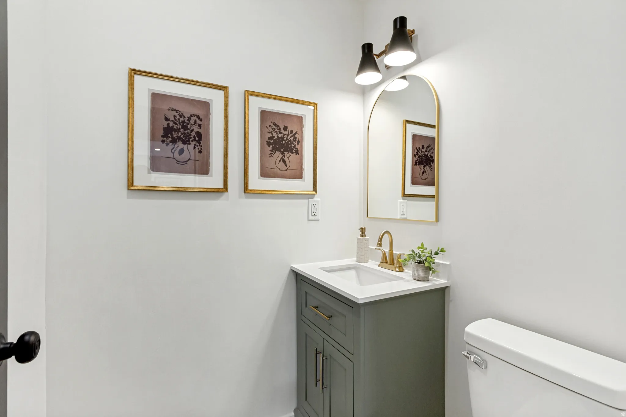 Vanity with a white countertop and integrated sink, a gold-framed arched mirror, and a two-light fixture