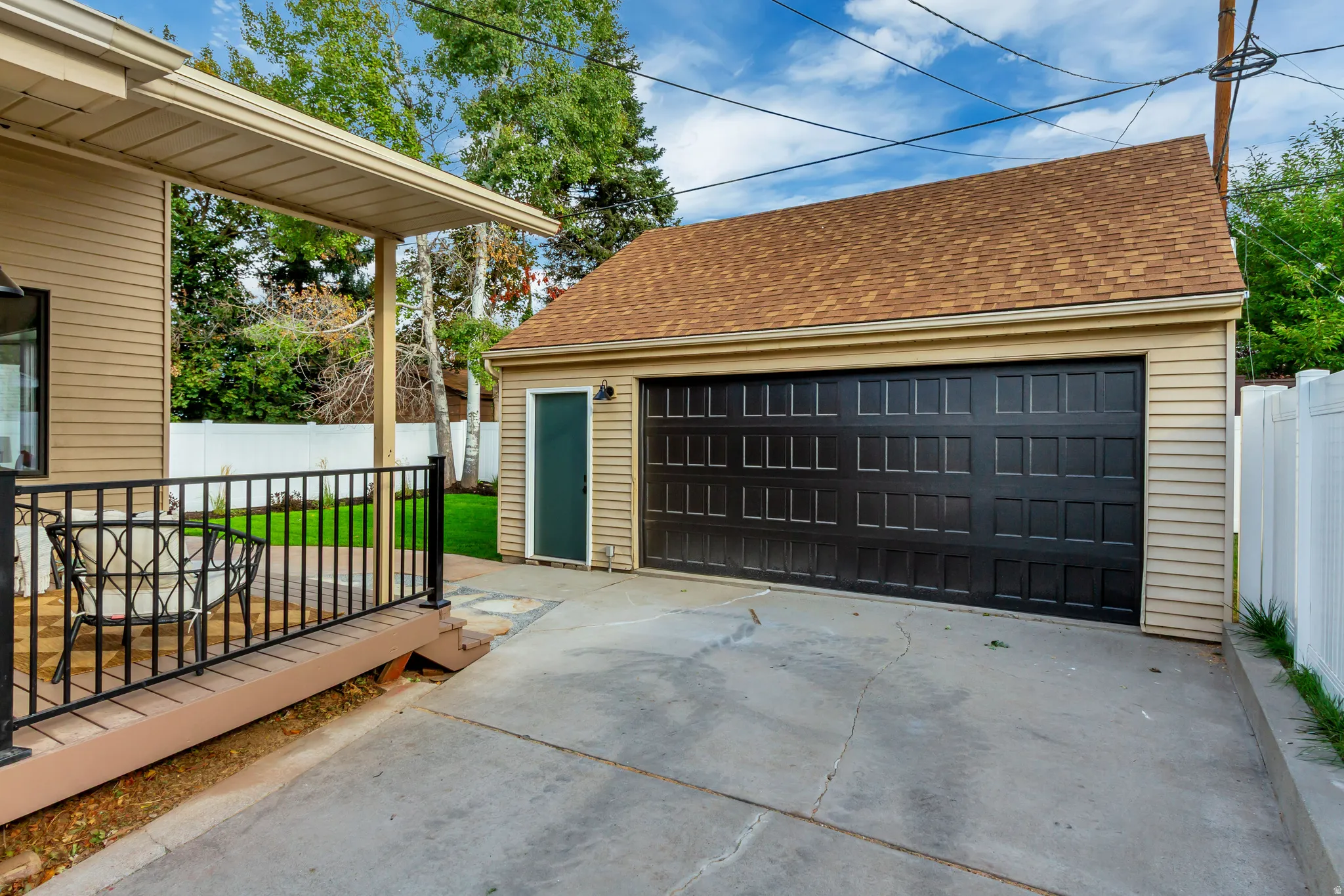 Attached two-car garage with a side entry door, concrete driveway, and a wood-finish deck with black metal railings